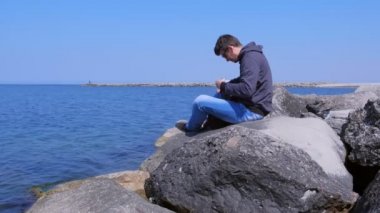Deniz kıyısında Adam selfie video çekmek için tripod ile sırt çantası telefon alır.