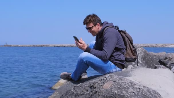 Man Traveler är glad över att få bra nyheter på smartphone sitter på Sea Beach. — Stockvideo