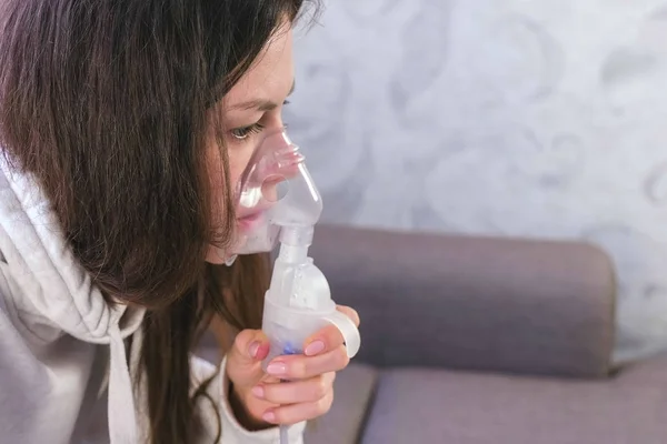 Per il trattamento utilizzare nebulizzatore e inalatore. Giovane donna che inala attraverso la maschera inalatore, primo piano del viso, vista laterale . — Foto Stock