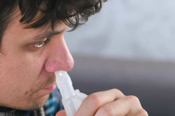 Zieke man via inhalator nozzle voor de neus inademen. Close-up gezicht, zijaanzicht. Vernevelaar en inhalator gebruiken voor de behandeling. — Stockfoto
