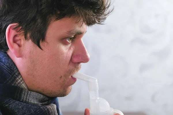 Use nebulizer and inhaler for the treatment. Sick man inhaling through inhaler nozzle for throat. Close-up face side view.