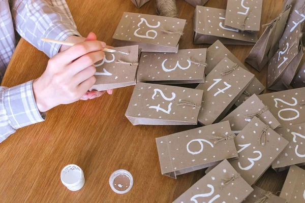 Una donna fa il calendario dell'avvento di Natale per i bambini. Scrive un numero sulla borsa con pennello e vernice bianca. Mani in primo piano . — Foto Stock