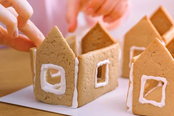 Womans hands make gingerbread houses glues details with sugar sweet icing. Cooking homemade gingerbread house.