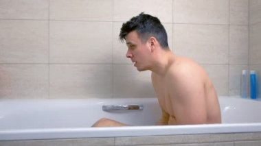 Adam küvette otururken başını yıkıyor..