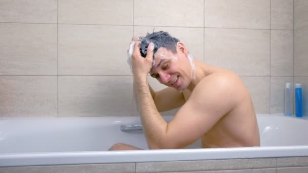 El hombre se lava la cabeza con champú y hace un Mohawk de pelos sentados en la bañera . — Vídeo de stock