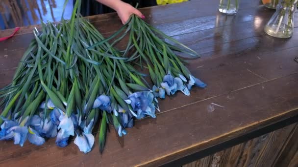 Kwiaciarnia kobieta sprawia, że bukiet z niebieskich kwiatów tęczówki na stole na sprzedaż w sklepie. — Wideo stockowe