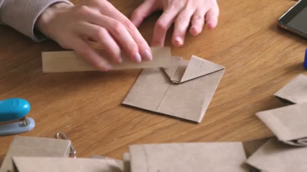 Una donna fa dei sacchetti di carta con carta kraft. Mani in alto. Piegare il righello . — Video Stock