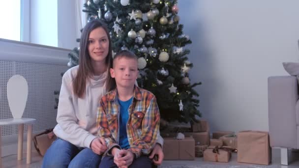 Retrato familiar de mamá e hijo sentados sonriendo cerca del árbol de Navidad en casa . — Vídeo de stock