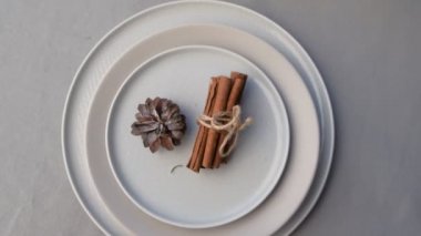 Çam kozalağı ve tarçın çubukları ile süslenmiş Noel yemeği için tabaklar.