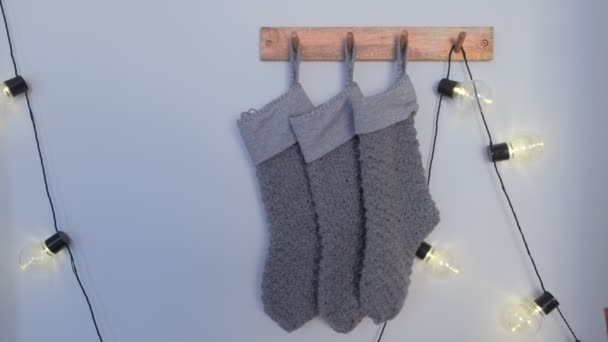 Різдвяні в'язані сірі шкарпетки на дерев'яних вішалках на білій стіні з гірляндою . — стокове відео