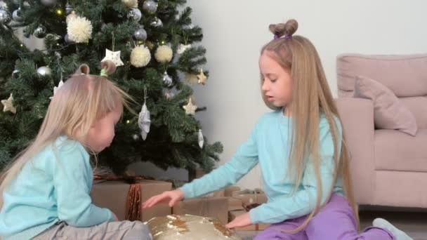 Twee meisjes zusters tekenen vingers op kussen met pailletten zitten in de buurt van kerstboom. — Stockvideo