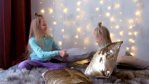 Két nővér játszik a párna arany flitter az ágyban a karácsonyi belső. — Stock videók