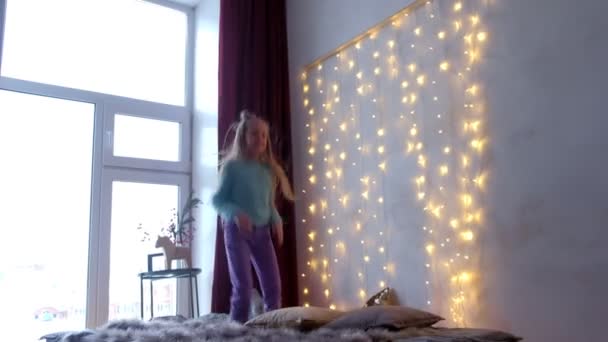 Boldog tini lány játszik jumping az ágyon a karácsonyi belső és nagy ablakokkal. — Stock videók