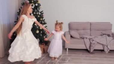 Güzel beyaz elbiseler içinde iki kız kardeş noel ağacının yakınında girdap ve dans.