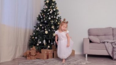 Tatillerde evde Noel ağacı yakınında dans beyaz elbiseli küçük sevimli kız.