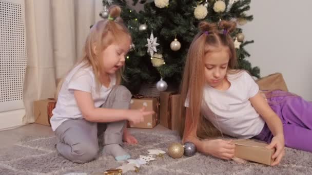 Dos hermanas jugando juntas juguetes y regalos sentadas cerca del árbol de Navidad . — Vídeos de Stock