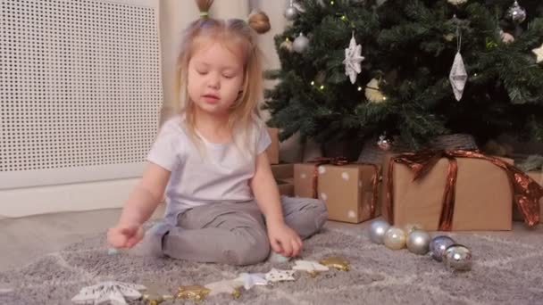 Linda niña contando estrellas y bolas sentadas cerca del árbol de Navidad en casa . — Vídeo de stock