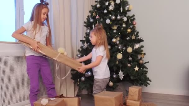 İki kız kardeş Noel ağacının yanındaki birbirlerinin hediye kutusunu alıp götürüyorlar.. — Stok video