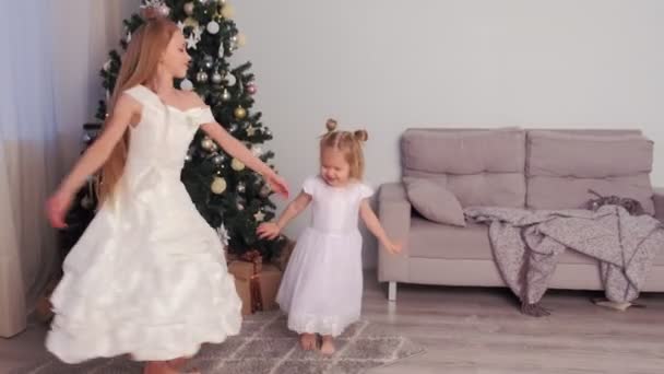 Two sisters in beautiful white dresses whirl and dance near Christmas tree. — Stock Video