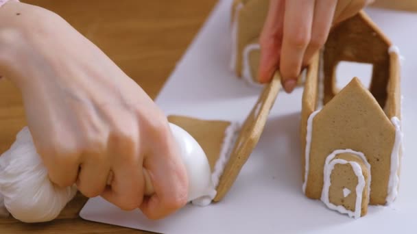 Frauenhände machen Lebkuchenhäuser mit zuckersüßem Zuckerguss verklebt. Kochen hausgemachte Lebkuchen Haus. — Stockvideo
