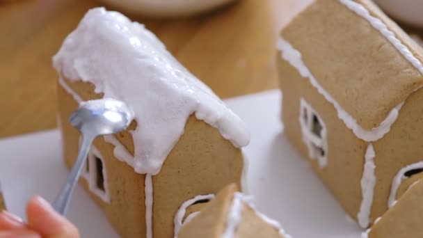 女性の手は砂糖甘いアイシングでジンジャーブレッドハウスの屋根を置きます。自家製ジンジャーブレッドハウスを調理. — ストック動画