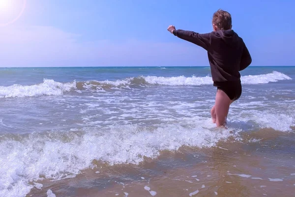 Niño juega y salta a través de las olas en la playa de arena de mar en el día de primavera ventoso . — Foto de Stock