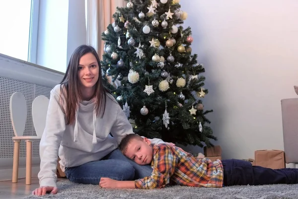 Anne oturma odasında evde Noel ağacı yakınında arka oğlu okşayarak, Yeni Yıl.