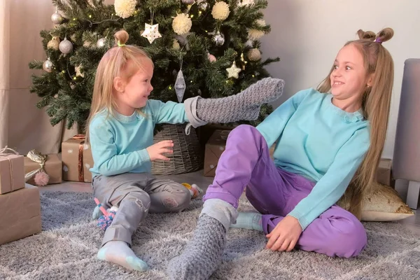 Kız kardeşler evde Noel ağacı yakınında oturan örme çorap ile oynuyor.