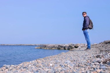 Sırt çantası ile Adam gezgin deniz taşları plajda ayakta denize bakıyor.