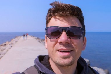 Portre adam görüntülü sohbetler selfie smartphone deniz plajı iskele yürüyüşleri ve gülümsüyor.