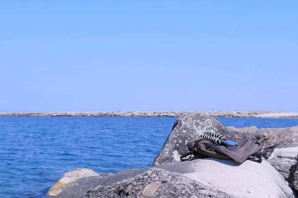 Plecak i smartfon na statywie na ogromnym kamieniu na plaży morskiej. — Zdjęcie stockowe