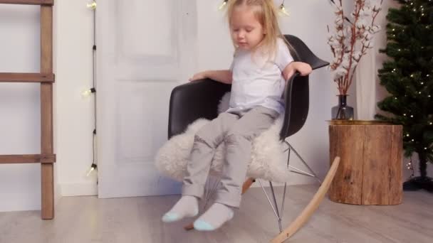 Kleine schattige kind meisje swingende op schommelstoel in kerst interieur thuis. — Stockvideo