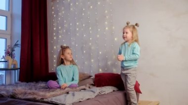 Kız kardeşi ile küçük sevimli kız evde yatak odasında şiir söyler, çocuklar.