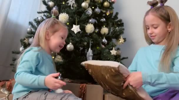 Retrato de dos hermanas niñas dibujan dedos en lentejuelas de almohada cerca del árbol de Navidad . — Vídeo de stock