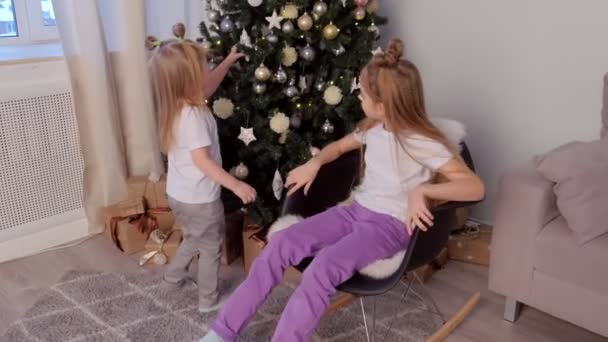 Crianças meninas irmãs olhando para brinquedos na árvore de Natal em casa na sala de estar . — Vídeo de Stock