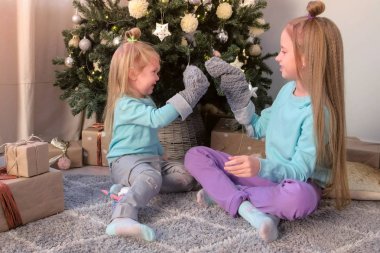 Kız kardeşler evde Noel ağacı yakınında oturan örme çorap ile oynuyor.