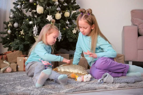 Zwei Mädchen Schwestern zeichnen Finger auf Kissen mit Pailletten sitzen in der Nähe von Weihnachtsbaum. — Stockfoto