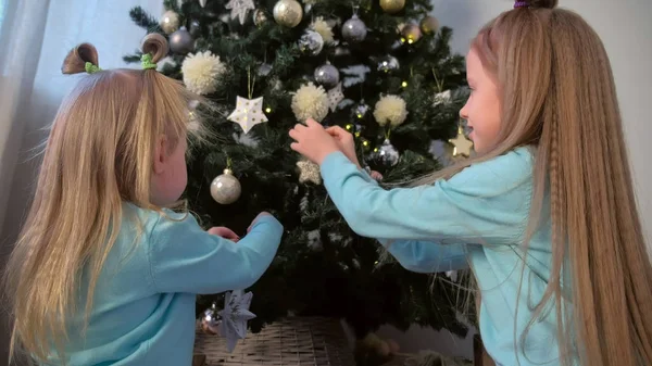 Dwie dziewczyny siostry decortaing Christmas Tree z zabawkami płatki śniegu i gwiazdki. — Zdjęcie stockowe