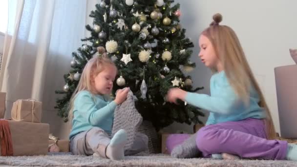 Δύο αδελφές που παίζουν χειροποίητα παιχνίδια και πλεκτές κάλτσες κοντά στο χριστουγεννιάτικο δέντρο. — Αρχείο Βίντεο