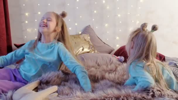 Barn flickor systrar kysser leka tillsammans på sängen i sovrum med girland. — Stockvideo