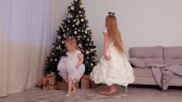 İki kız kardeş kızlar güzel beyaz elbiseler Noel ağacının yanında dans ediyorlar.. — Stok video