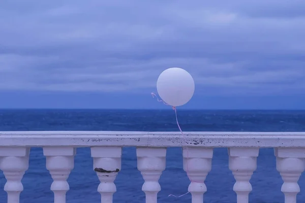 Ballon blanc dans le vent attaché à la clôture sur le front de mer par une journée nuageuse . — Photo