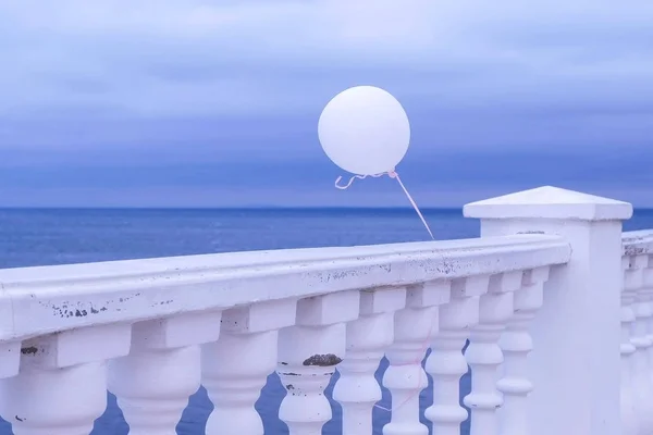 Ballon blanc dans le vent attaché à la clôture sur le front de mer par une journée nuageuse . — Photo