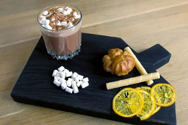 Cocoa dengan marshmallow dalam kaca batu pada nampan hitam kayu dengan kue dan lemon. Tampilan samping close-up . — Stok Foto
