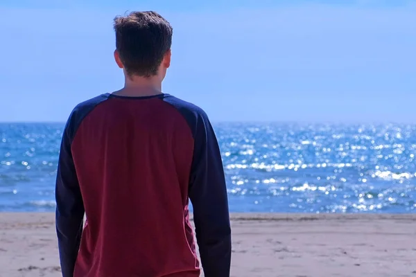 Jeune homme regarde la mer sur la plage de sable de mer, vue arrière . — Photo