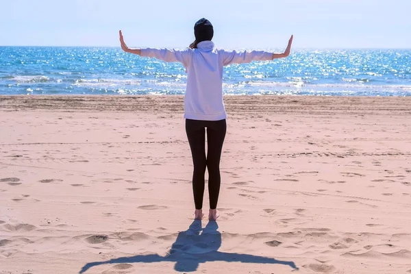 女性は、側面に砂の海のビーチの腕の上に立って、ヨガの運動バックビューを作ります. — ストック写真