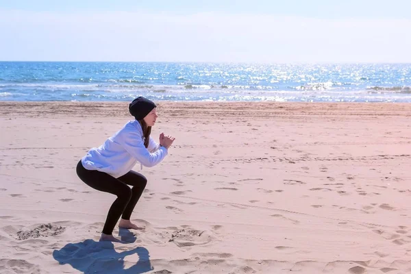 女性は海の砂浜フィットネス屋外スポーツエクササイズトレーニングでスクワットを行います. — ストック写真