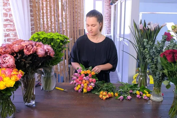Kwiaciarnia kobieta sprawia, że bukiet z małych kolorowych róż działa w kwiaciarni. — Zdjęcie stockowe