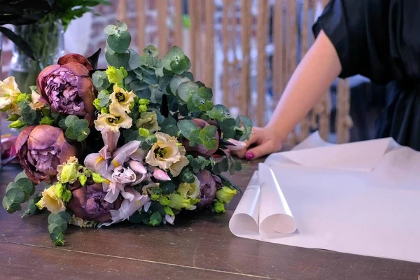 Florista faz buquê de flores prepara papel para embalagem na loja, mãos closeup . — Fotografia de Stock