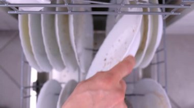 Mans el bulaşık makinesine kirli bir tabak koyar ve mutfak ile paletler iter.